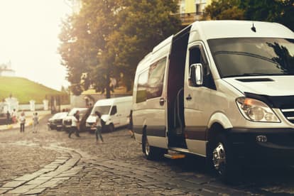 A white minibus parked in a cobblestone lot